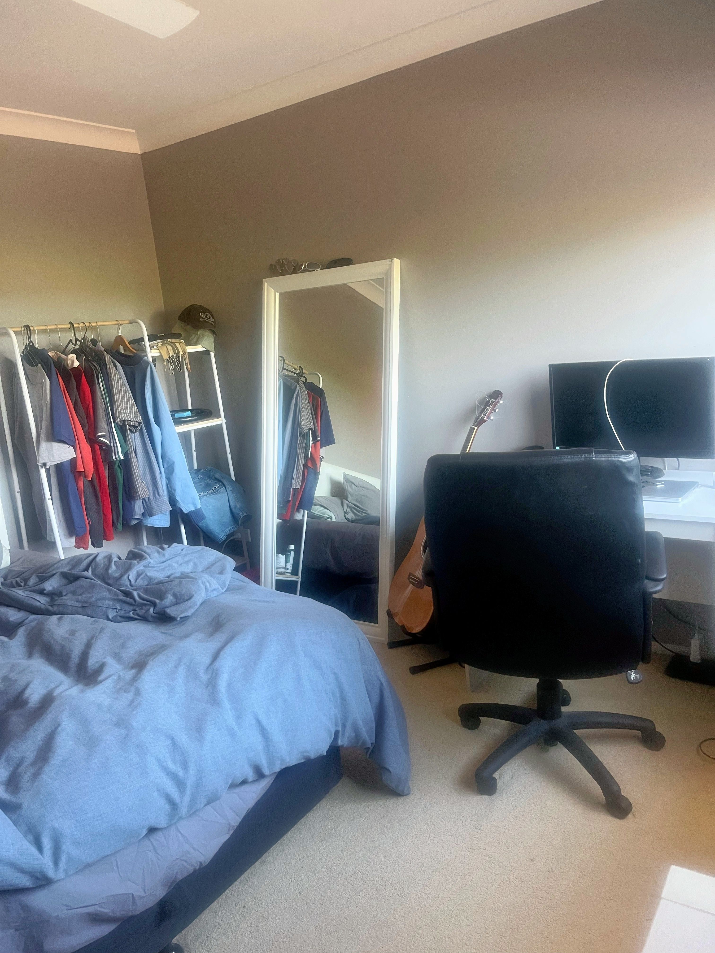 A bedroom with a made bed, laptop and belongings placed neatly, showing an adult living space inside a family home.
